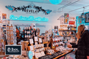 A vibrant boutique store interior filled with colorful, handmade art, jewelry, and gifts. A neon sign on the wall reads "From Louisville with Love" above displays of local artisan goods. A woman browses the merchandise, creating a cozy and welcoming shopping atmosphere.
