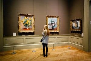 Woman with long blonde hair is looking at paintings at a museum.