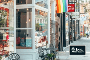 A sidewalk outside of shops in the NuLu district of Louisville, with a Pride flag and small bistro tables.