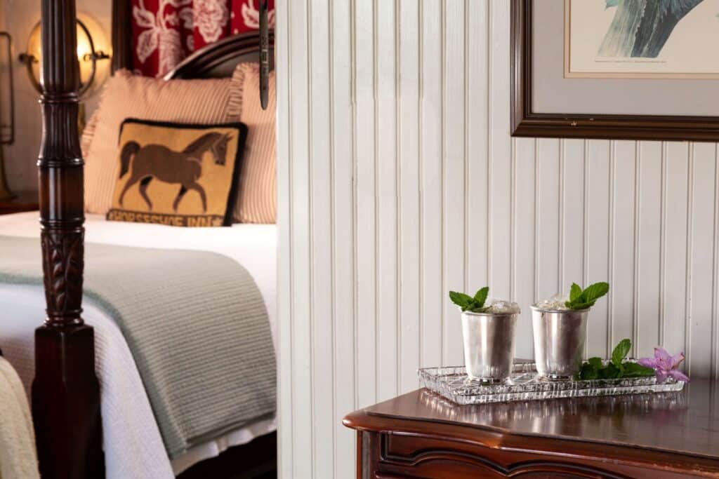 Cozy bedroom scene with a wooden bedpost, striped pillow, and a silver tray holding two mint-garnished cups on a wooden table.