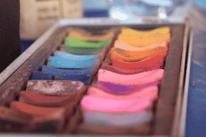 A rainbow assortment of chalk sticks in a tray.