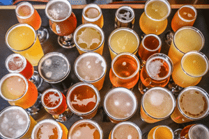 Tops of multiple beers varying in color from dark brown to golden yellow in various clear glassware.