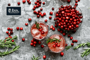 Two glasses with ice, cranberries, and a red drink are on a gray table covered in fresh cranberries.