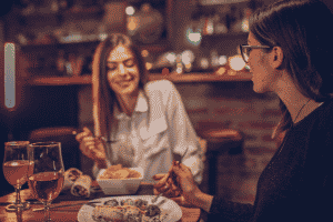 Two women eating dinner at a dimly lit restaurant with wooden decor.