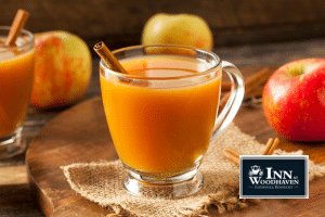 Clear glass mug filled with apple cider and garnished with a cinnamon stick, with apples in the background.