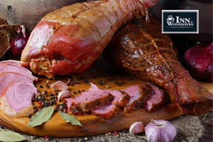 Two smoked turkey legs resting on top of a wood cutting board with a few slices of cut meat and a head of garlic