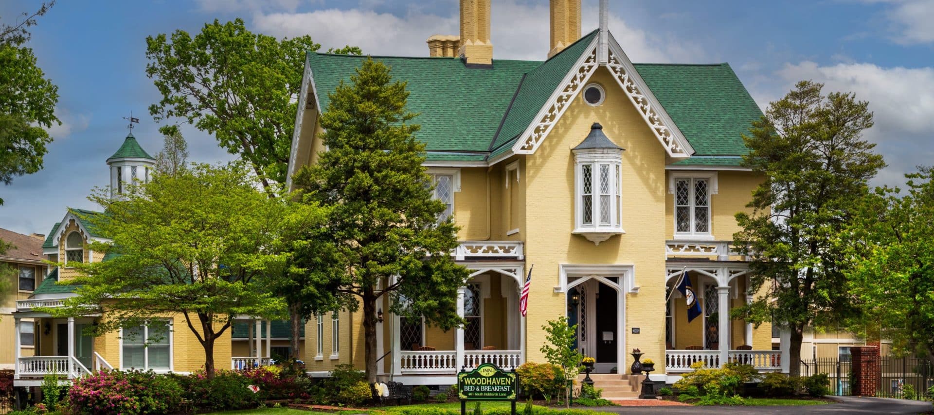 Front view of the yellow gothic mansion with green roofs and white gingerbreading. Rose Cottage is to the left in the image and the main house is in the center and the right.