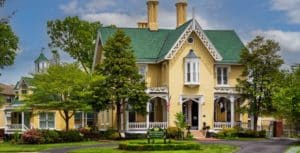 Front view of the yellow gothic mansion with green roofs and white gingerbreading. Rose Cottage is to the left in the image and the main house is in the center and the right.