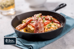 Black skillet on a blue towel filled with a Louisville Hot Brown sandwich topped with bacon