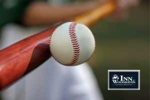 Wooden baseball bat striking a white baseball with red stitching.