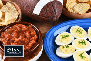 Wooden table with an American football, blue plate of deviled eggs, and a brown bowl of chili.