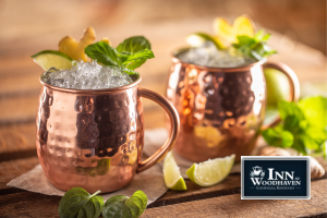 Two copper Moscow mule cups on a wooden table, garnished with lime and mint leaves