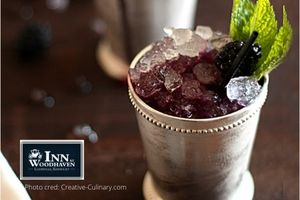 Blackberry mint julep drink over ice in a silver mint julep cup with a sprig of green mint.