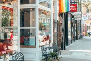 Sidewalk and storefronts with small bistro tables outside.