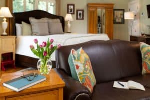 brown leather loveseat next to a table with journal and purple tulips with king sized bed in the background