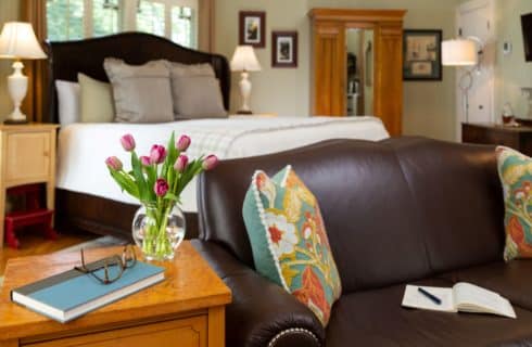 brown leather loveseat next to a table with journal and purple tulips with king sized bed in the background