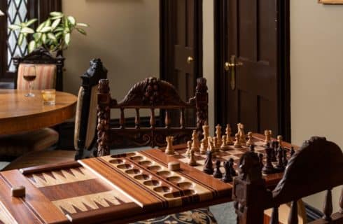 custom made wood game table with chess game being playes and a table in the background with a glass of bourbon.