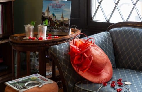 Derby themed picture with a Derby book, two mint juleps, a derby hat and a horseshoe.