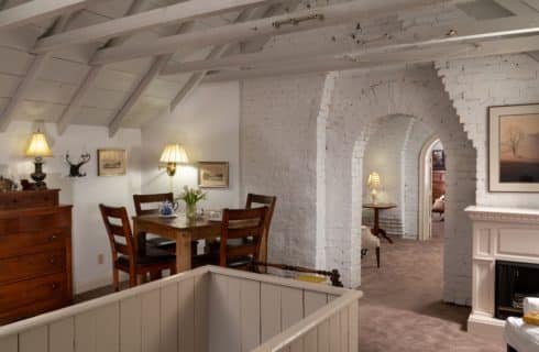 Spacious attic sitting area with a counter-height table and four chairs, a brick arched doorway in the center and a faux fireplace on the right