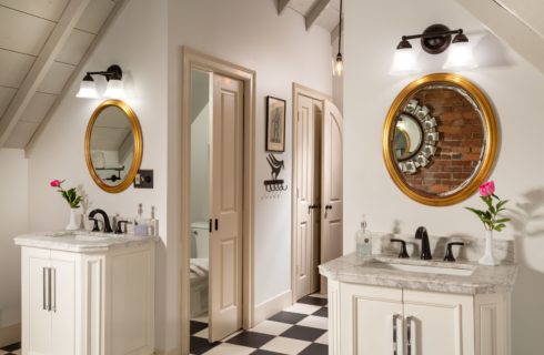 Picture showing scale of bathroom with dual vanities with mirrors and floral arrangements and the private commode area, vaulted ceilings and a black and white checkerboard tile floor