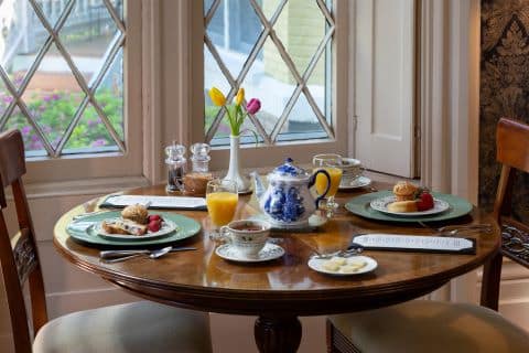 Breakfast setting in the dining room with juice, pastries and a teapot. In front of a gothic style window.