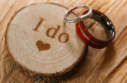 Wooden ring slab engraved with “I do” and a heart, with two rings resting on top.