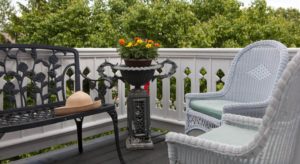 White wicker patio chairs and wrought iron bench on balcony with green trees in the background