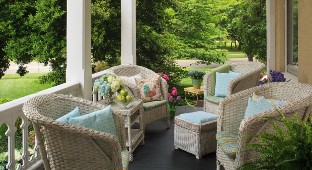 Front porch with white wicker patio furniture and view of green bushes and trees