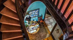 Winding dark wooden staircase with reddish argyle stair runner and view to the entryway below