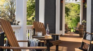 long view of 2 porches with brown wood adirondack chairs and rocking chairs, stand on front porch with ice bucket and refreshments