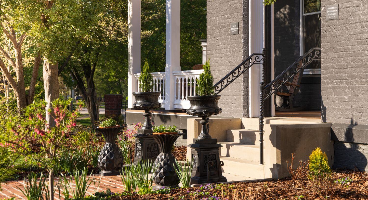 view of lush garden beside porch on gray house with metal planters along walkway