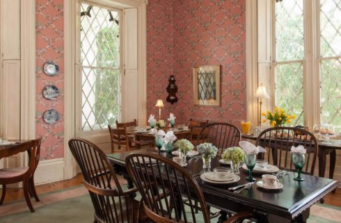 Large dining room with pink wallpaper, hardwood flooring, large gray area rug, and multiple dark wooden tables and chairs