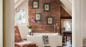 Large bathroom with white soaker tub, terra cottage brick accent wall, and tan wicker chaise