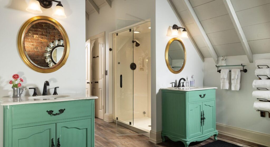 2 separate single bowl sinks with mint green cabinets, gold framed circular mirrors above , walk-in shower with planking floors