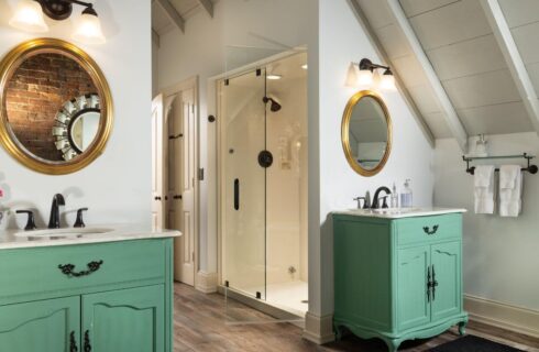 2 separate single bowl sinks with mint green cabinets, gold framed circular mirrors above , walk-in shower with planking floors