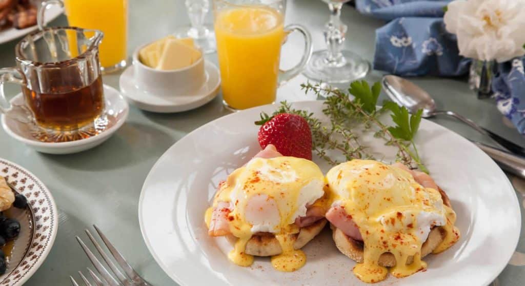 White plate with eggs benedict, large strawberry, and glass of orange juice