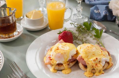 White plate with eggs benedict, large strawberry, and glass of orange juice