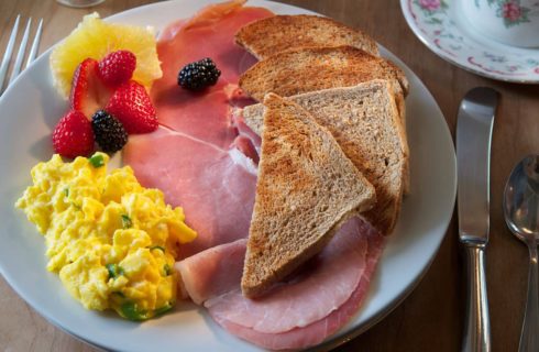 White plate with scrambled eggs, ham, wheat toast, strawberries, and blackberries