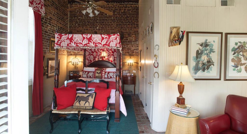 Bedroom with dark wooden four-poster canopy bed, red and white bedding, white-paneled walls, and red leather chair