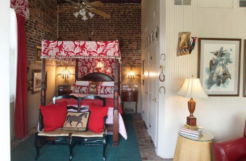 Bedroom with dark wooden four-poster canopy bed, red and white bedding, white-paneled walls, and red leather chair