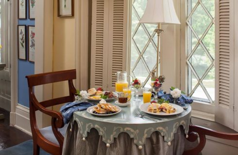 Two wooden chairs at small round table with multiple plates each with a different breakfast dish
