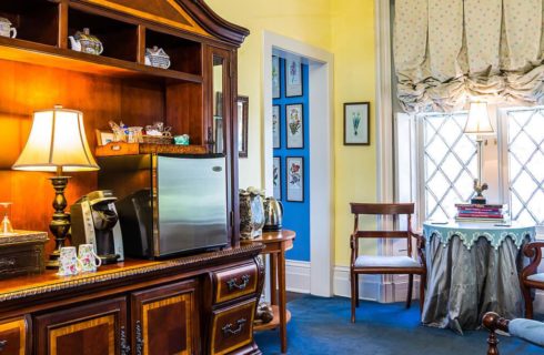 Large room with yellow walls, blue carpeting, small sitting area with wooden chairs, and large wooden entertainment center with alcohol, coffee maker, and mini fridge