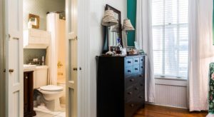 Bedroom with hardwood flooring, white and teal walls, dark wooden dresser, and view into bathroom with white tile flooring