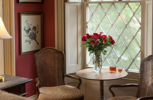 Sitting area with two brown wicker, wood, and upholstered chairs, wooden table, and glass vase with red roses