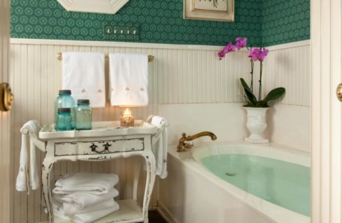 Bathroom with large white soaker tub, white paneled walls, and antique cart holding white towels