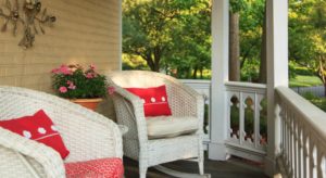 Front porch with white wicker rocking chairs and bright red pillows and green trees in the background