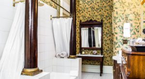 Large bathroom with wallpaper walls, white tile flooring, tub and shower, and dark wooden vanity with marble top