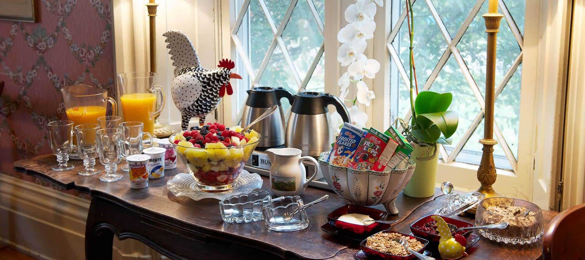 Large wooden table set up with a continental breakfast including cereal, fruit, and orange juice