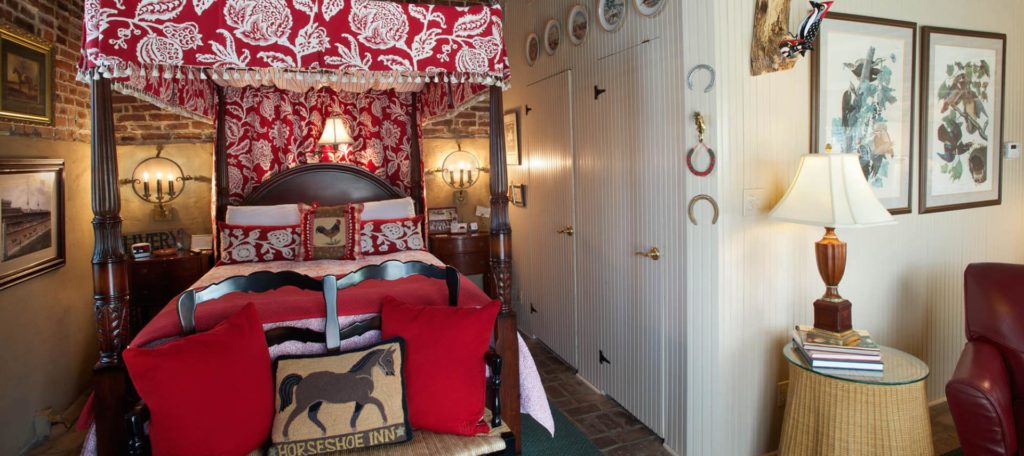 Bedroom with dark wooden four-poster canopy bed, red and white bedding, white-paneled walls, and red leather chair