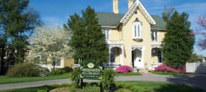 Exterior view of the property painted cream with white trim surrounded by green trees, shrubs, and grass